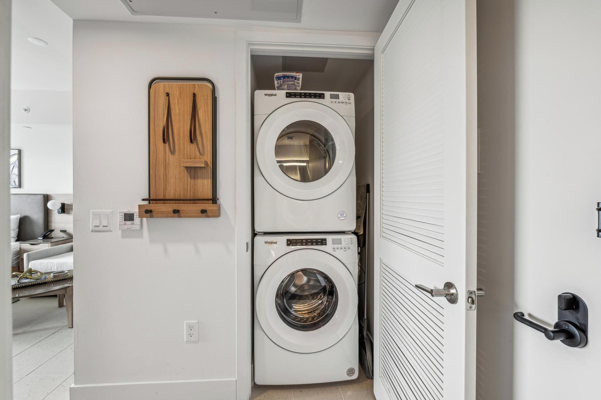 A compact laundry room with two stacked front-loading washing machines, a wooden cabinet, and a door with a modern handle.