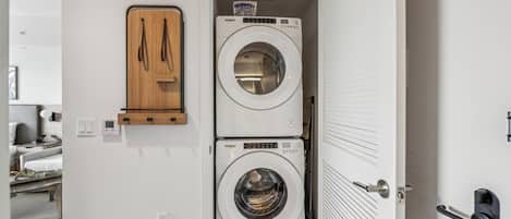 Une petite buanderie équipée de deux machines à laver à chargement frontal superposées, d’un meuble en bois et d’une porte dotée d’une poignée moderne.