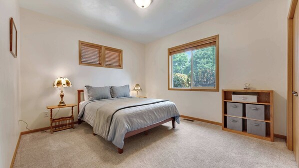 A bedroom with a bed, two bedside lamps, a window, and a built-in storage unit.