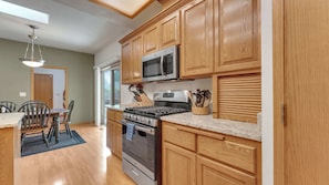 A kitchen with wooden cabinets, a stainless steel stove, a microwave, and a dining area with a table and chairs.