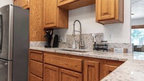 A kitchen with wooden cabinets, a stainless steel refrigerator, a coffee maker, and a sink with a faucet. - Evergreen Haven - Spacious Retreat Near the Best of Eugene (Eugene)