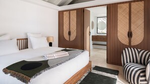 Una camera da letto con un letto, una lampada da comodino, una poltrona a righe e un armadio con ante intrecciate.