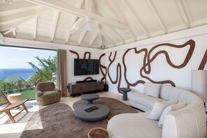 A modern living room with a large TV, comfortable seating, and a view of the ocean. - Villa Scarlett (2 bedrooms) (Saint Barthélemy)