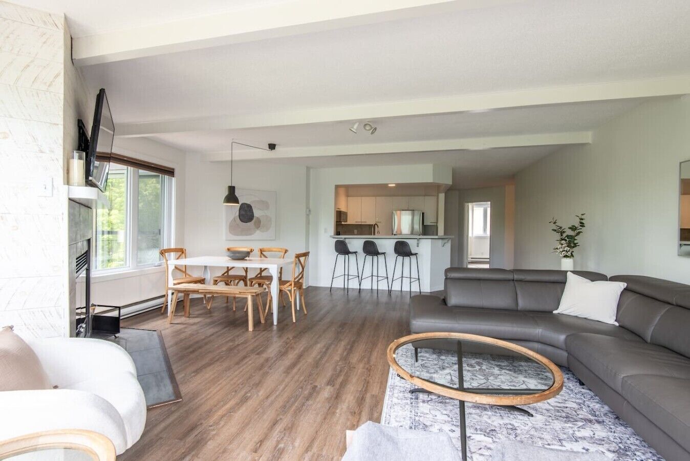 A modern living room with a grey sofa, a round coffee table, and a dining area with wooden chairs.