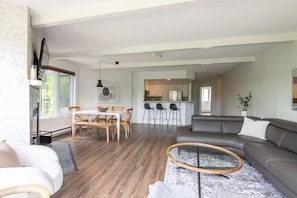 Ein modernes Wohnzimmer mit einem grauen Sofa, einem runden Couchtisch und einem Essbereich mit Holzsesseln.