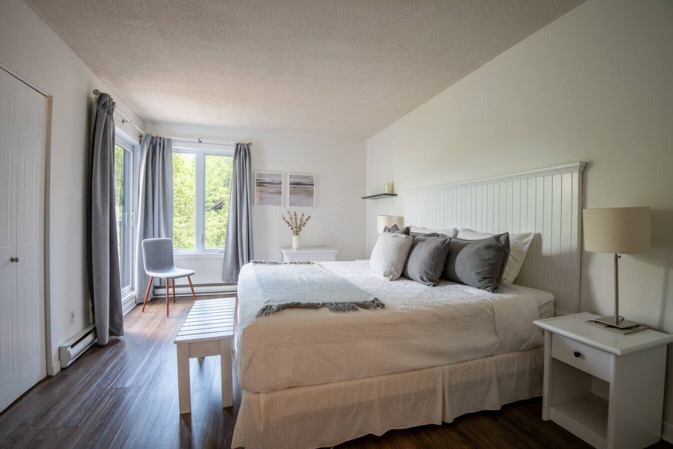 Une chambre à coucher avec un grand lit, des tables de chevet, une chaise et une fenêtre avec des rideaux.
