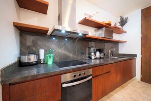 A modern kitchen with a dark marble countertop, stainless steel appliances, wooden cabinets, and built-in shelves. - Your Home in the Mayan Jungle (Tulum)