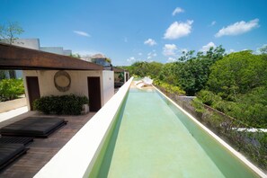 A long, narrow pool with a wooden deck on one side and a lush green landscape on the other. - Your Home in the Mayan Jungle (Tulum)