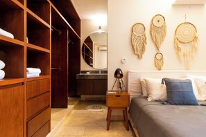 A bedroom with a wooden wardrobe, a bedside table with a lamp, a bed with pillows, and wall-mounted macramé decorations. - Your Home in the Mayan Jungle (Tulum)