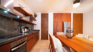 A modern kitchen with wooden cabinets, a stainless steel refrigerator, and a dining area with a wooden table and chairs. - Your Home in the Mayan Jungle (Tulum)