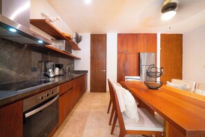 A modern kitchen with wooden cabinets, a stainless steel refrigerator, and a dining area with a wooden table and chairs. - Your Home in the Mayan Jungle (Tulum)