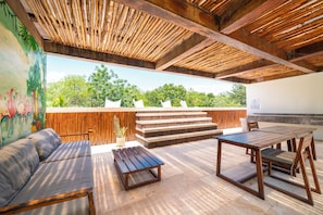 An outdoor patio with wooden furniture, a mural, and a view of greenery. - Your Home in the Mayan Jungle (Tulum)