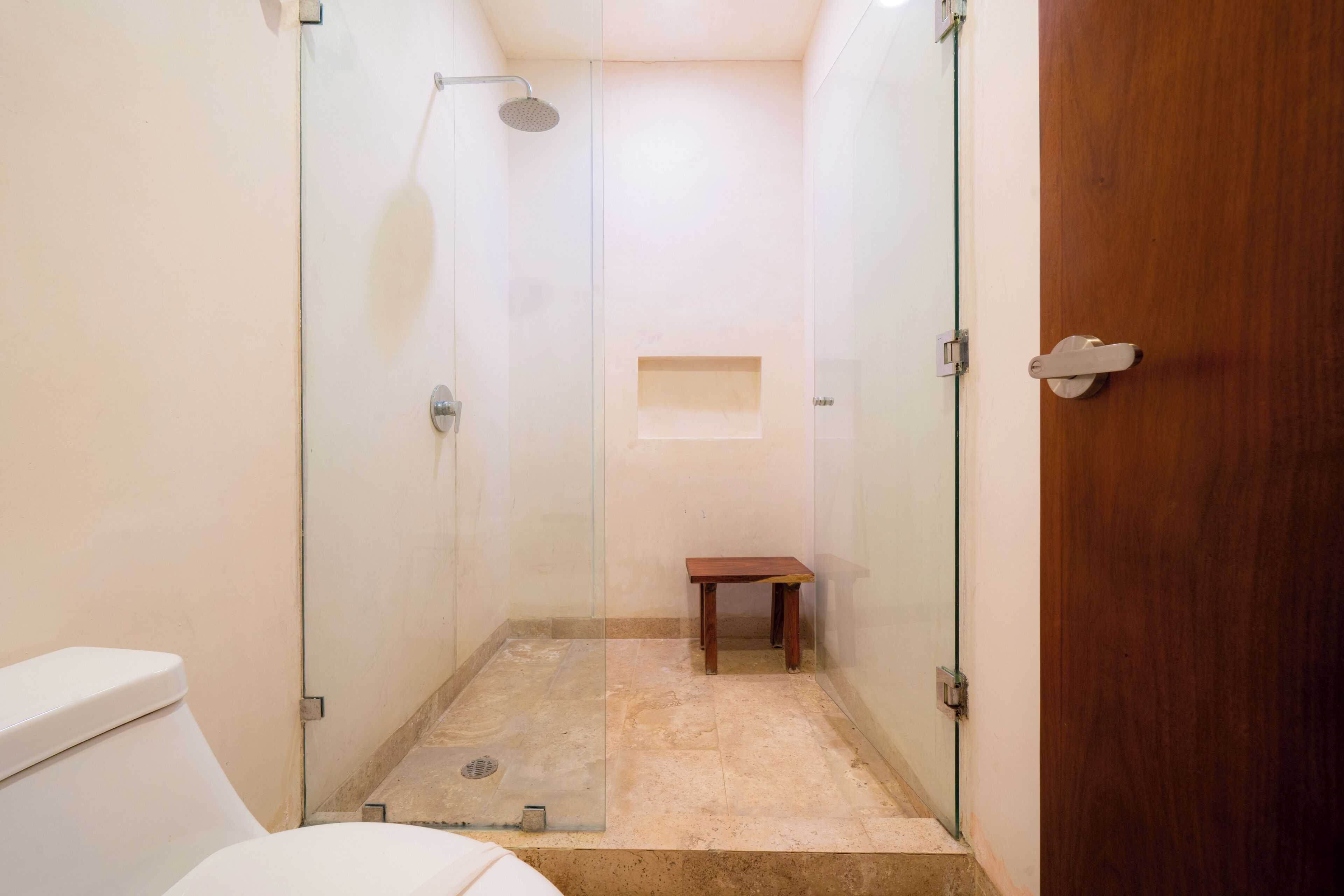 A glass-enclosed shower area with a wooden bench, a toilet, and a door.