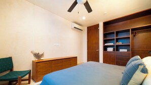 A bedroom with a bed, a wooden dresser, a bench, and a built-in wardrobe with shelves. - Your Home in the Mayan Jungle (Tulum)