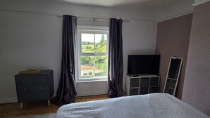 A bedroom with a bed, a dresser, a TV, and a window with curtains. - West Acre Cottage - sleeps 5 guests in 3 bedrooms (Westacre)