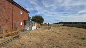 A brick building with a small attached structure, a fenced yard, and a wooden fence. - West Acre Cottage - sleeps 5 guests in 3 bedrooms (Westacre)