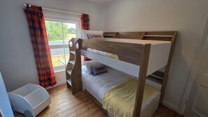 A bunk bed with a wooden frame and white bedding, a window with curtains, and a small white storage unit. - West Acre Cottage - sleeps 5 guests in 3 bedrooms (Westacre)