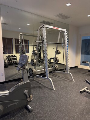 Une salle de sport équipée de machines de cardio, de postes d’entraînement en musculation et d’haltères.