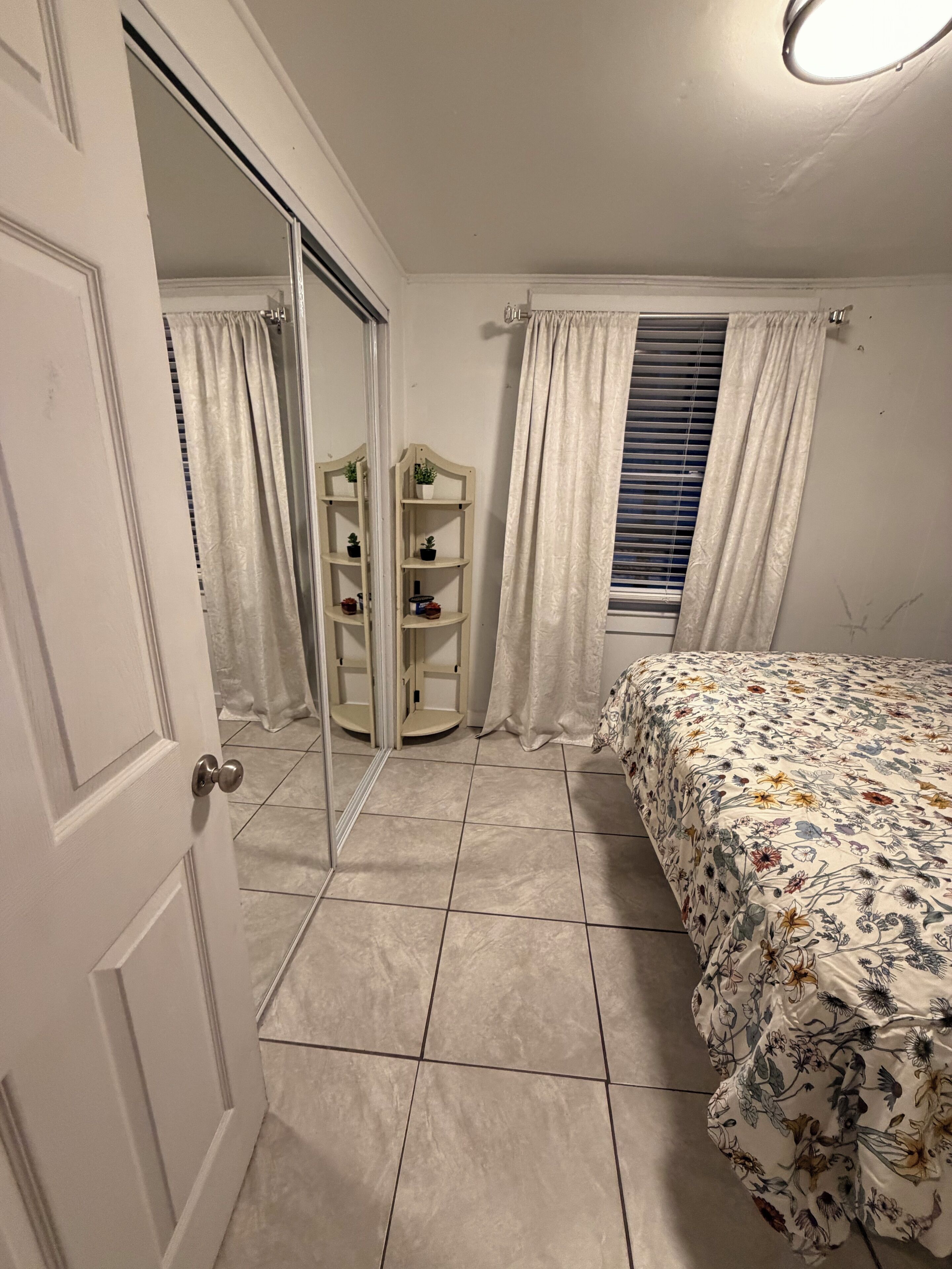 Une chambre à coucher avec un lit, une armoire, un miroir et une fenêtre avec des rideaux.