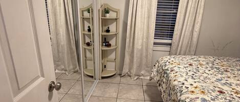 A bedroom with a bed, a wardrobe, a mirror, and a window with curtains.