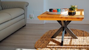 Un salón moderno con un sofá, una mesa de centro de madera con una bandeja de tazas y una planta en maceta.