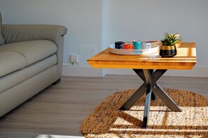 Ein modernes Wohnzimmer mit einer Couch, einem Holztisch mit einer Kaffeetassen-Servierplatte und einem Blumentopf.