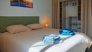 Habitación de hotel con cama, mesita de noche, lámpara, armario y un cuadro en la pared.