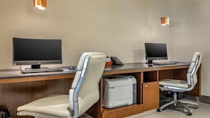 Un espace de bureau moderne comprenant deux bureaux, chacun équipé d’un écran d’ordinateur, d’un clavier et d’un téléphone. On y trouve également deux chaises de bureau à roulettes, et une imprimante est visible sur l’un des bureaux.