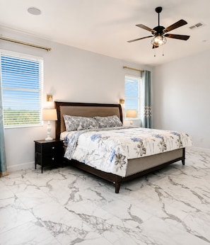 A bedroom with a bed, nightstands, a ceiling fan, and a window with blinds. - Luxury 5BR Retreat with Private Pool in Buckeye (Buckeye)