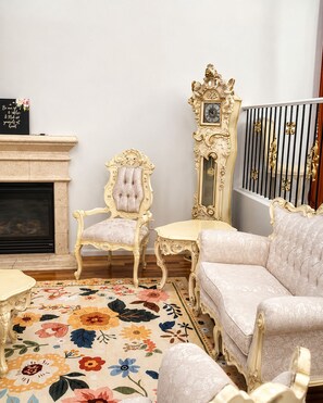 A room with a fireplace, a floral rug, a tufted armchair, a sofa, and a mirror with ornate gold detailing. - Luxury 5BR Retreat with Private Pool in Buckeye (Buckeye)