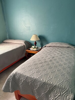 Ein Zimmer mit zwei Betten, einem Nachttisch mit Lampe und einem kleinen Tisch mit Blumenarrangement.