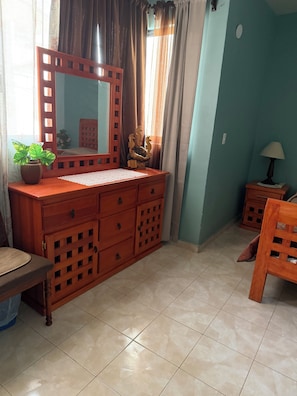 Ein Zimmer mit einem Holzkasten, einem Spiegel, einem Blumentopf, einem kleinen Tisch und einem Stuhl.