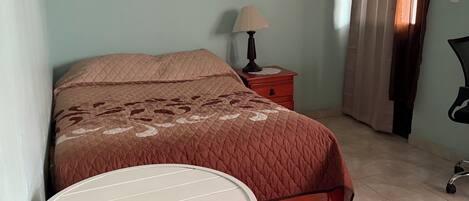 A bedroom with a bed, a nightstand, a lamp, a chair, and a table.