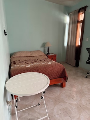 A bedroom with a bed, a nightstand, a lamp, a chair, and a table.