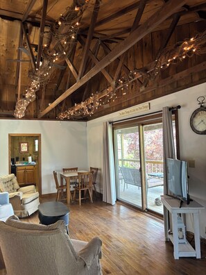 A cozy living room with wooden beams, a television, and a dining area with chairs and a table.