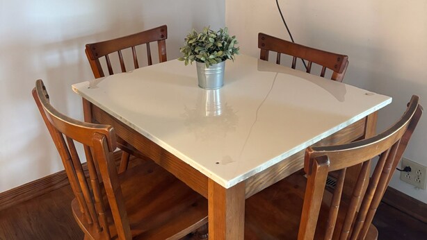 Une table à manger avec quatre chaises en bois, une plante en pot et une prise électrique visible sur le mur.