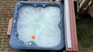 Un bain à remous avec une terrasse en bois et un mur de briques en arrière-plan.