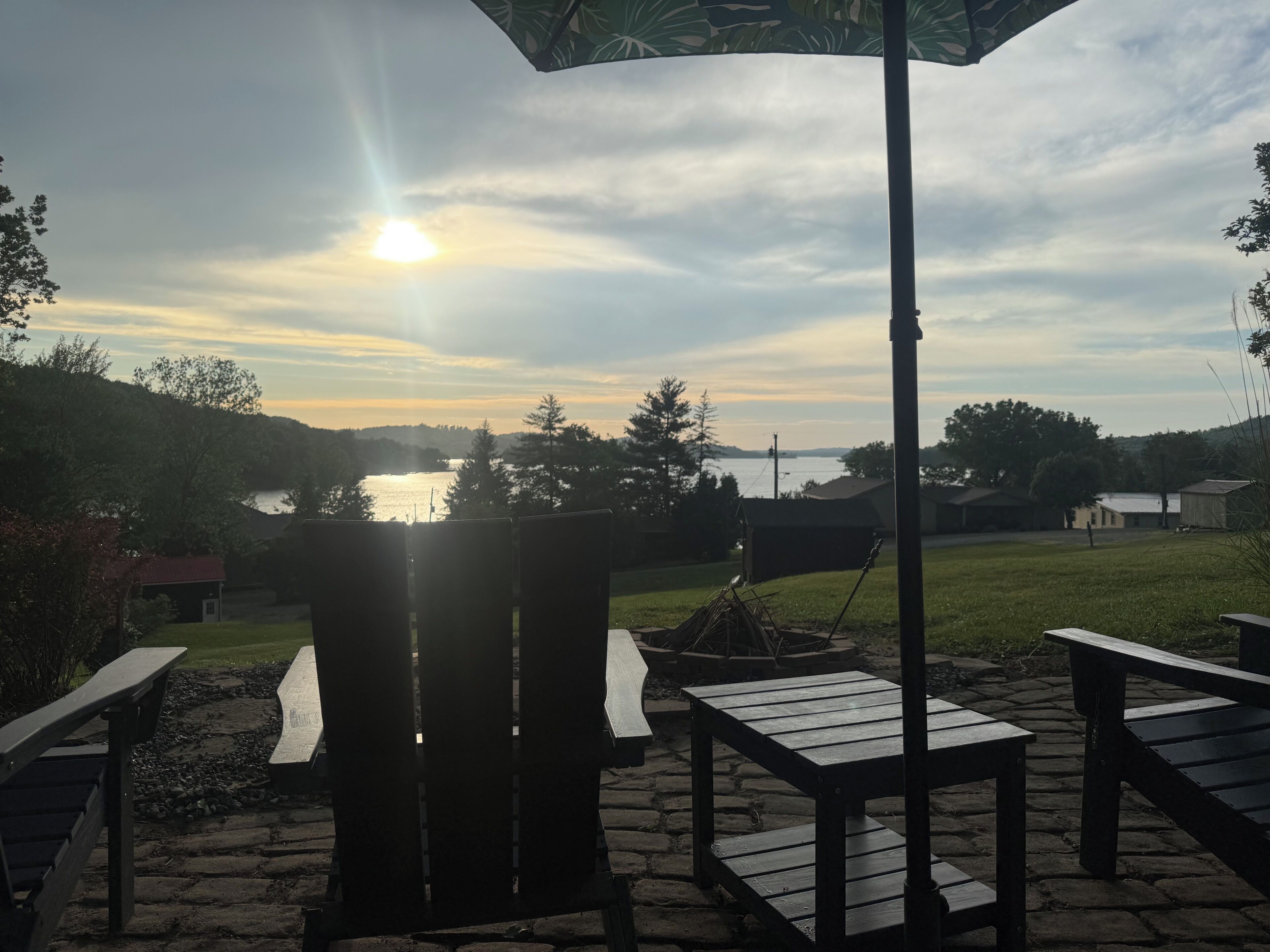 Un espace extérieur aménagé avec des chaises et des tables, une terrasse en bois et une vue sur un lac au coucher du soleil.