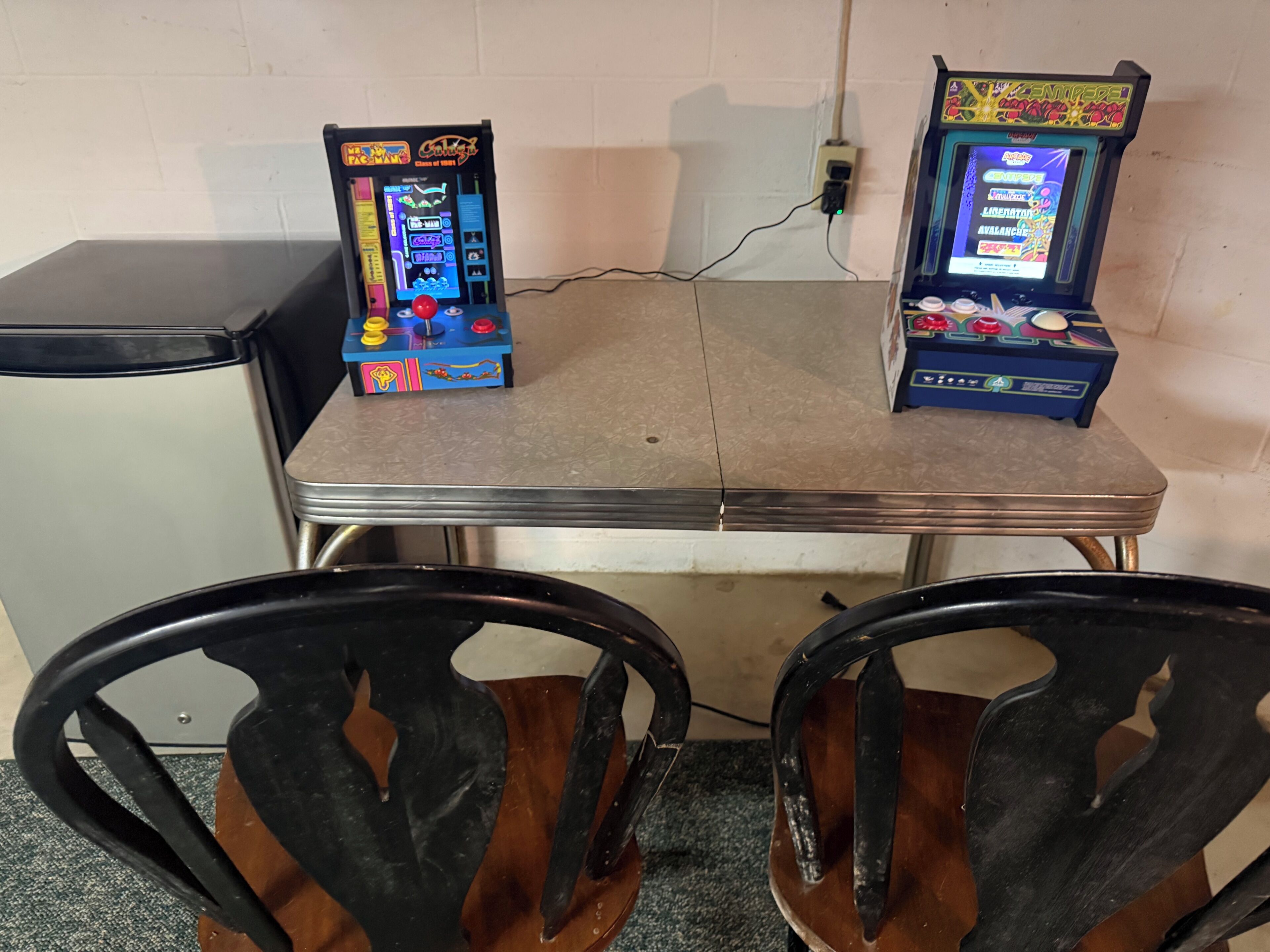 Zwei Spielautomaten auf einem Tisch, davor Stühle.