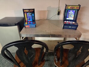 Two arcade machines on a table with chairs in front.