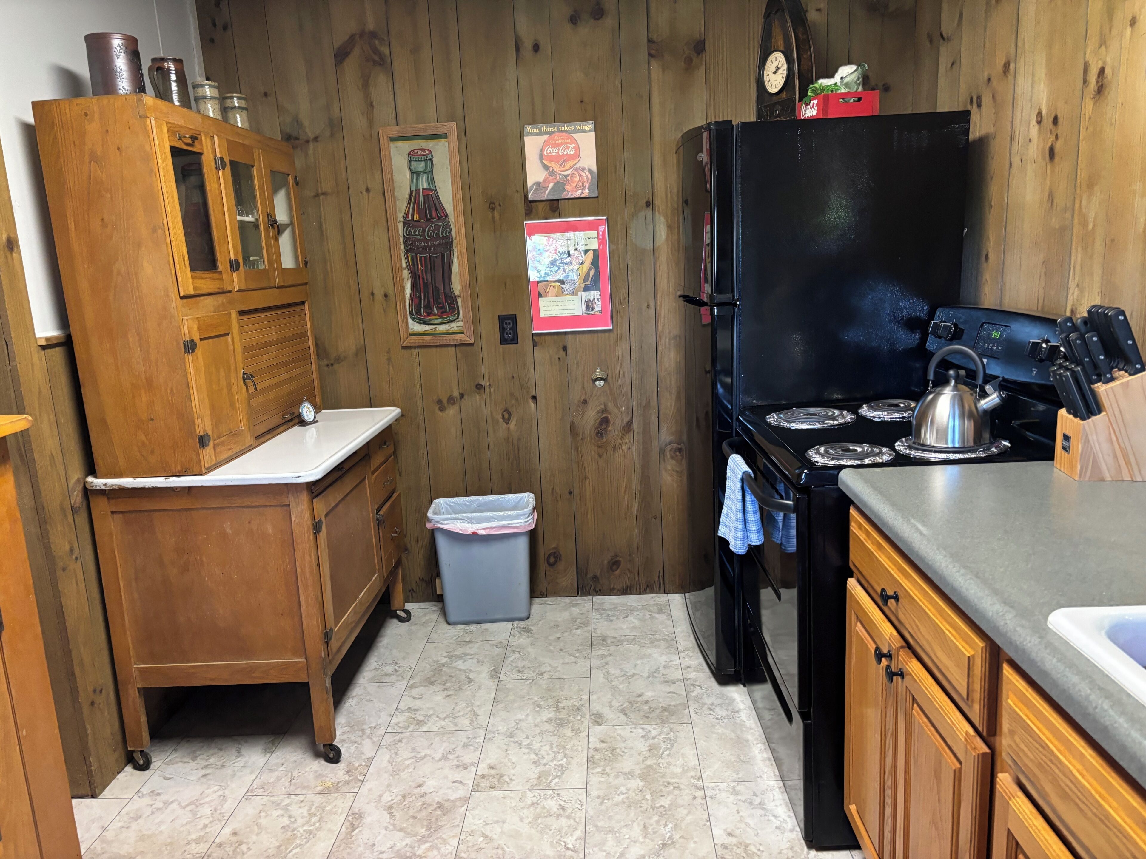 Une cuisine avec des meubles de rangement en bois, une cuisinière noire, un évier et une poubelle.