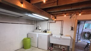 A laundry room with a washing machine, dryer, sink, and green trash bin.