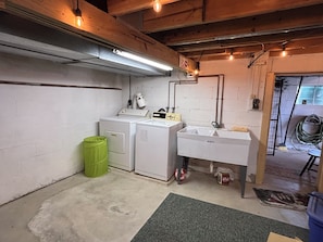 A laundry room with a washing machine, dryer, sink, and green trash bin.
