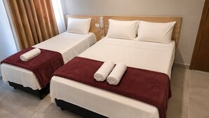 A hotel room with two beds, each with a white mattress and a red blanket. There are white pillows on each bed, and a wooden headboard is visible.