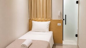 A hotel room with a bed, a bedside table, an air conditioning unit, and a door.