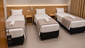 A hotel room with three single beds, a wooden headboard, a bedside table with a phone, and a door with a room number sign.