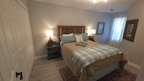 A bedroom with a bed, two bedside tables with lamps, a nightstand, a door, and a window with curtains. - Cozy 3-bedroom home near KSU, Braves and Lake Point SPorts Complex (Marietta)