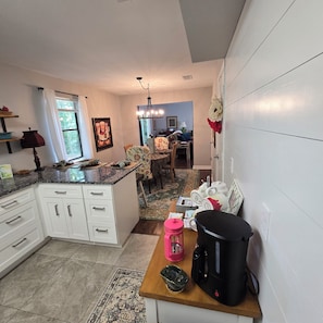 A kitchen with a central island, a dining area with a chair, and a coffee maker on the counter. - Cozy 3-bedroom home near KSU, Braves and Lake Point SPorts Complex (Marietta)
