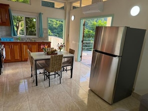 Una cocina con una mesa de comedor, sillas, un refrigerador y una ventana que ofrece vistas a zonas verdes.