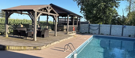 Un área de piscina con muelle de madera, mobiliario exterior y jacuzzi.